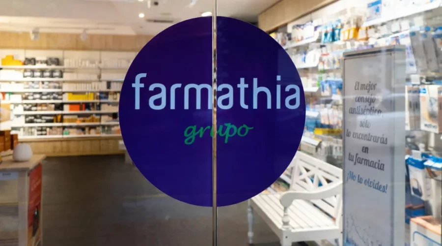 Logo de "farmanthia grupo" sobre pastilla de fondo azul en la puerta automática de cristal de entrada a una farmacia