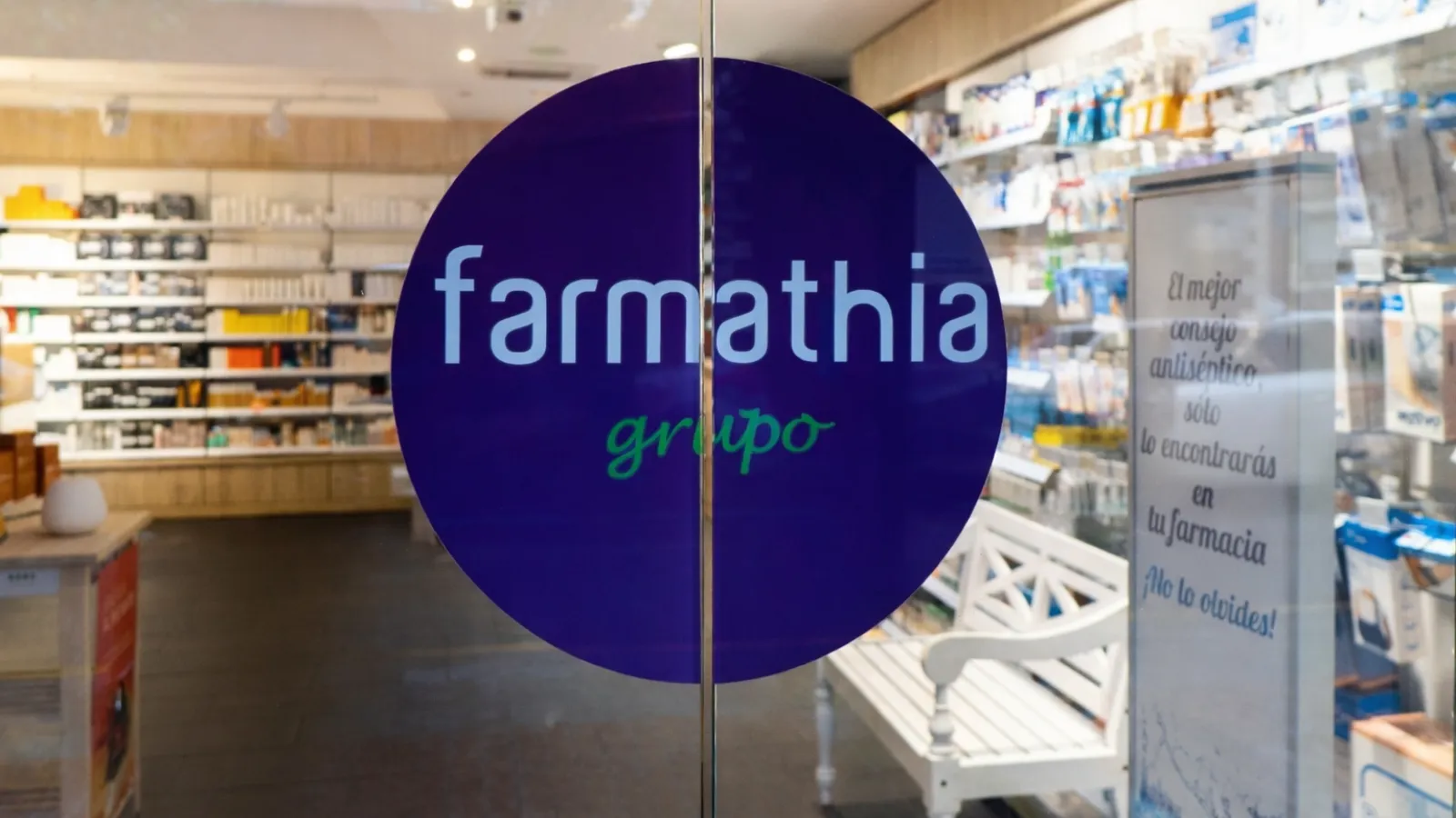 Logo de "farmanthia grupo" sobre pastilla de fondo azul en la puerta automática de cristal de entrada a una farmacia